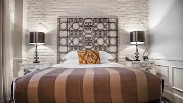Uma cama com cabeceira estampada, duas mesas de cabeceira com abajures e um edredom listrado.