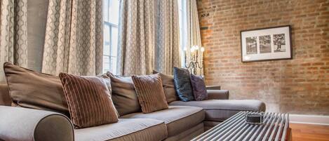 A living room with a sofa, patterned curtains, a brick wall, and a framed picture.