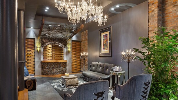 A modern lounge area with a sofa, two armchairs, a chandelier, a potted plant, and a framed picture on the wall.