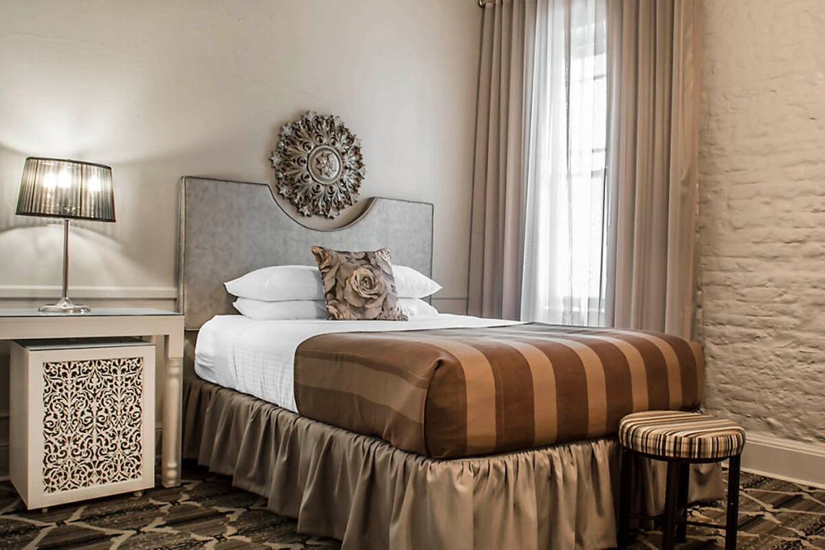A neatly arranged hotel room with a bed, a bedside table with a lamp, a decorative wall piece, and a window with curtains.