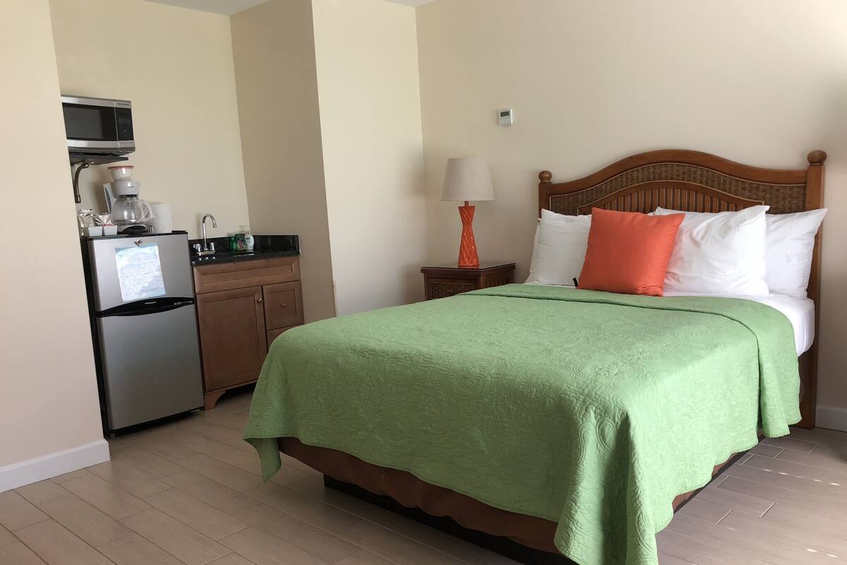 Een hotelkamer met een bed, nachtkastje, lamp, magnetron, koelkast en een kleine keukenhoek.