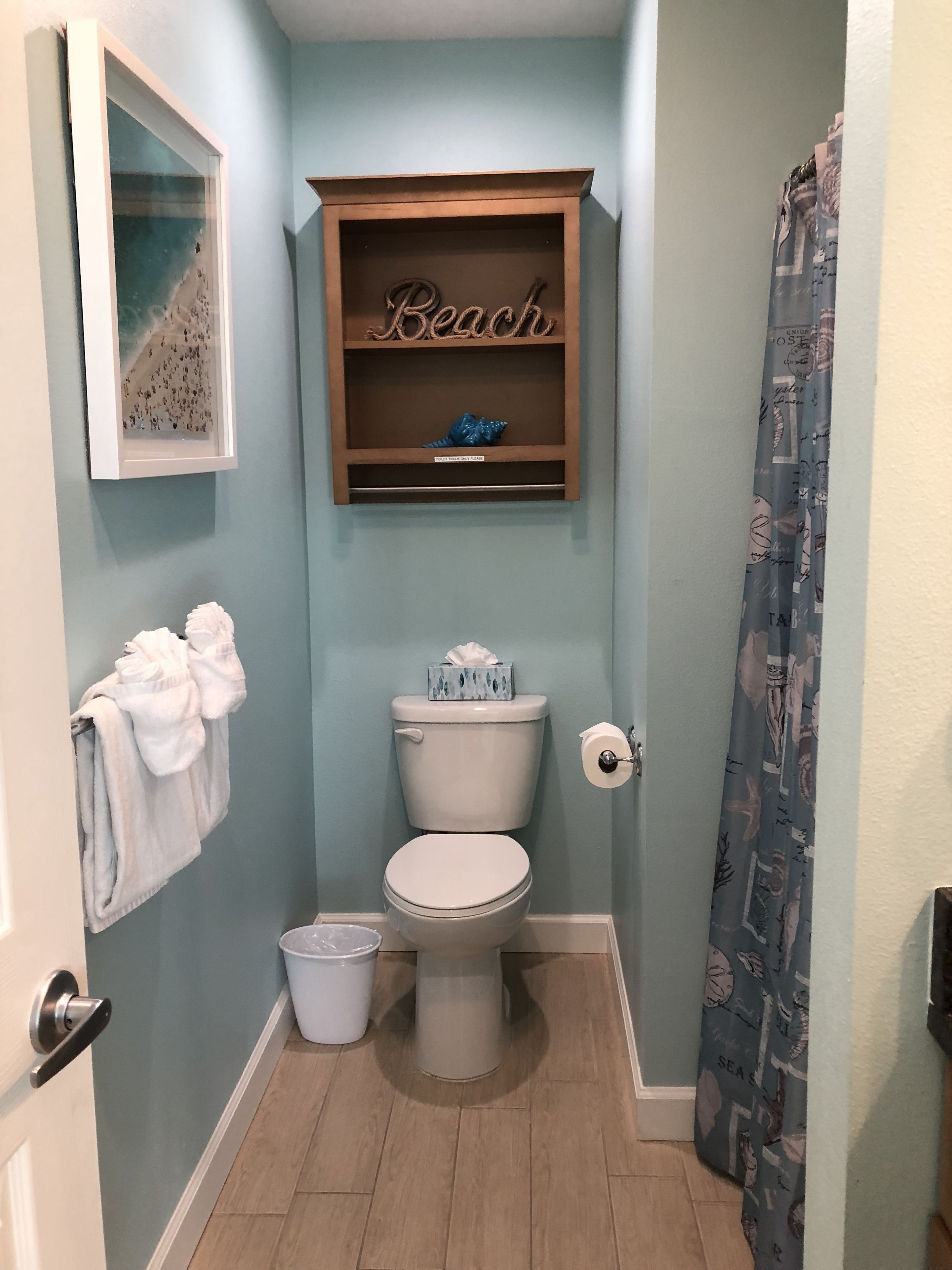Ein Badezimmer mit Toilette, einer kleinen Ablage mit einem Schild mit der Aufschrift 'Beach', einem gerahmten Bild an der Wand und einer Duschvorhang.