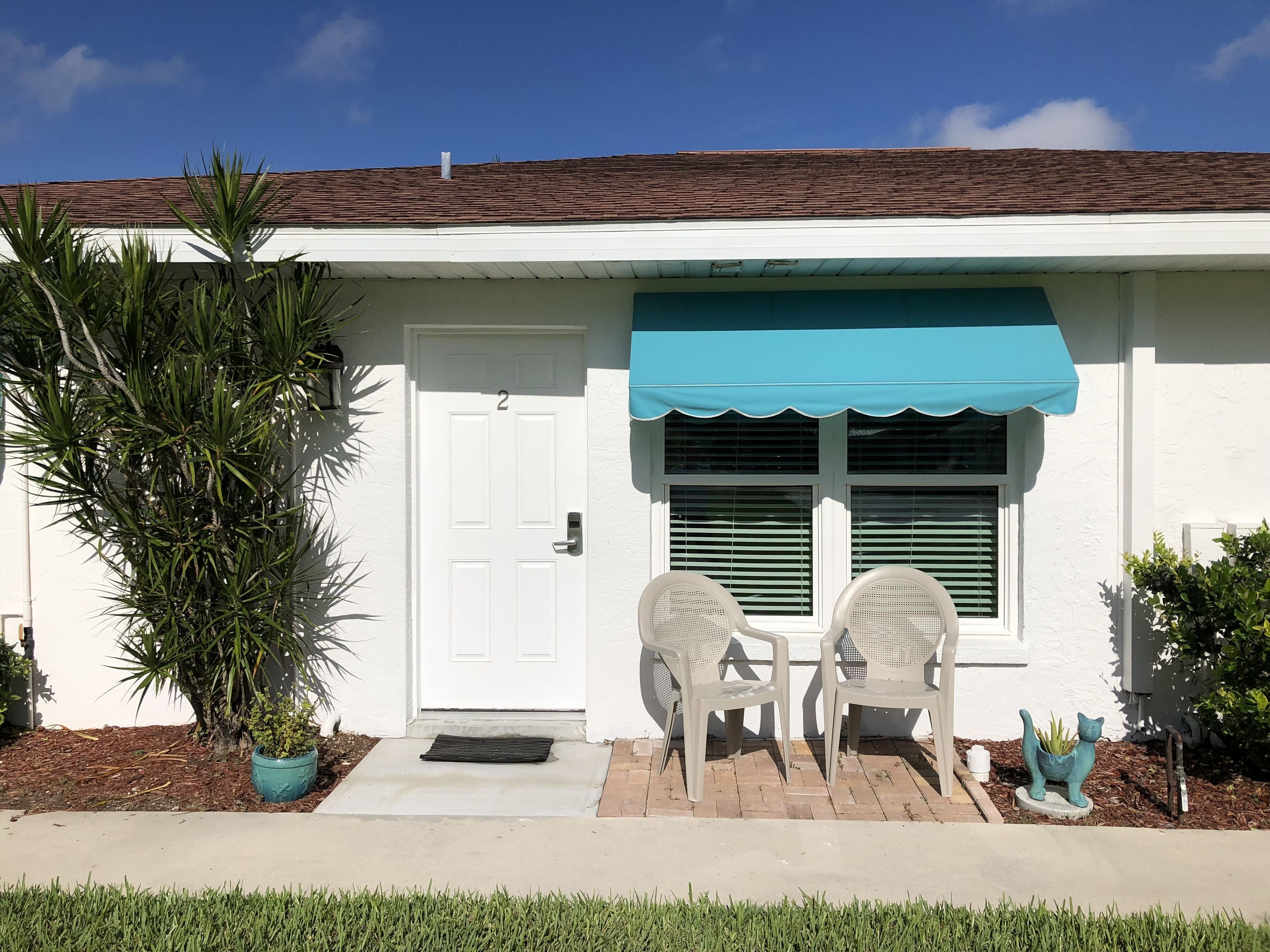 A white building with a brown roof, a teal awning, and a door marked with the number 2.