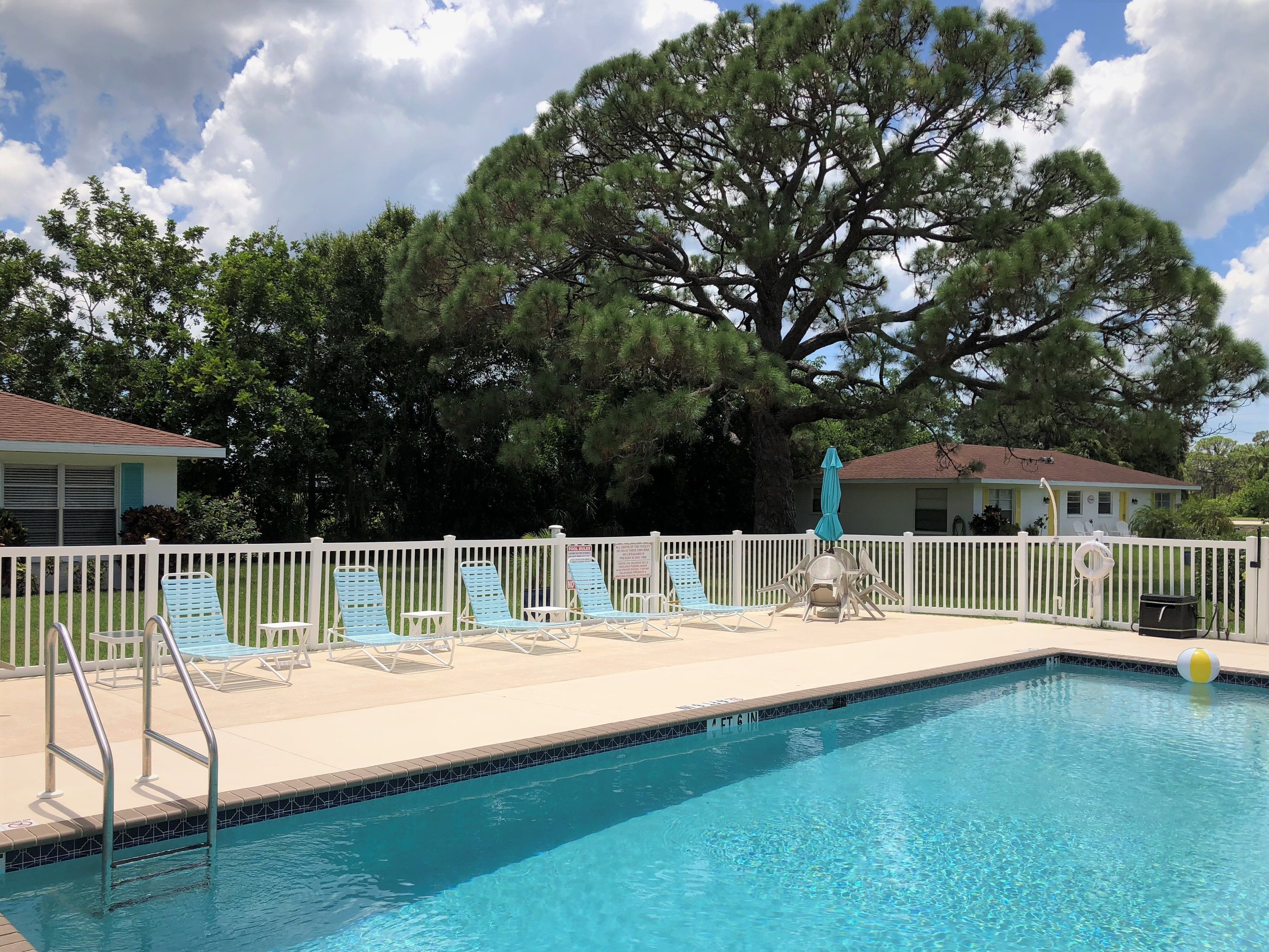 Een zwembad met ligbedden en een witte afrastering.