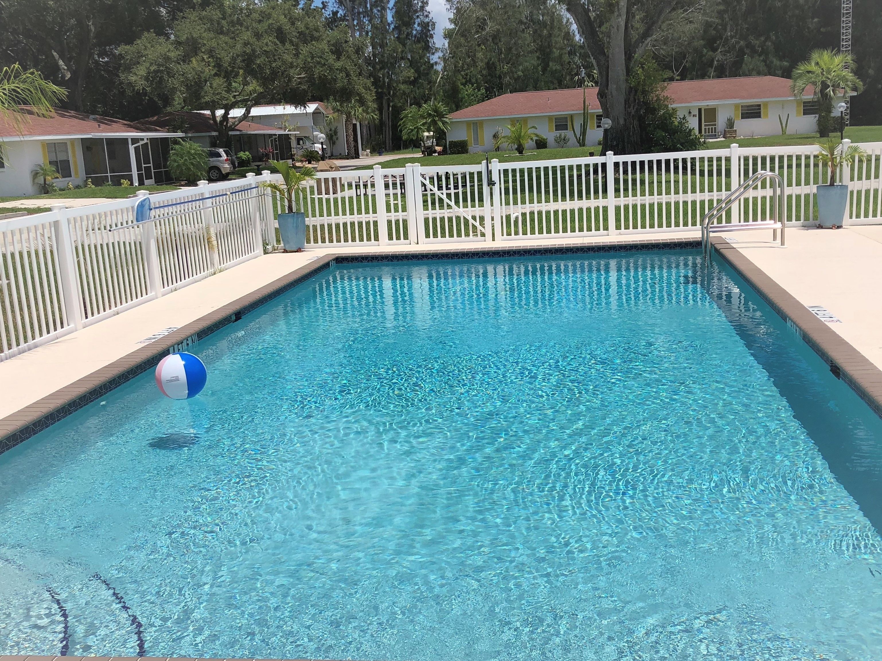 Ein rechteckiger Pool mit klarem, blauem Wasser, umgeben von einem weißen Zaun und einer kleinen Liegefläche.