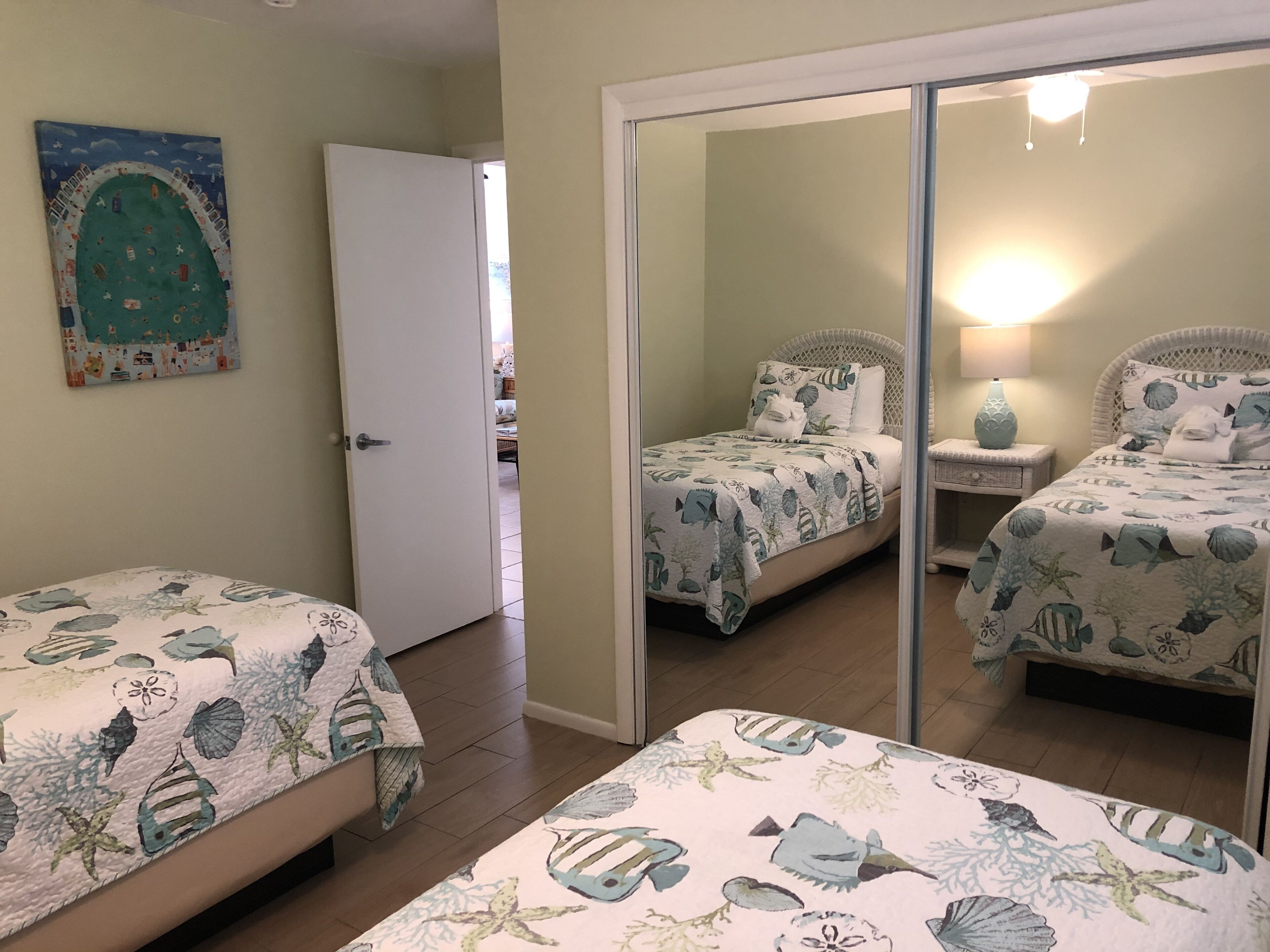 A bedroom with two beds, a large mirror, and a door leading to another room.