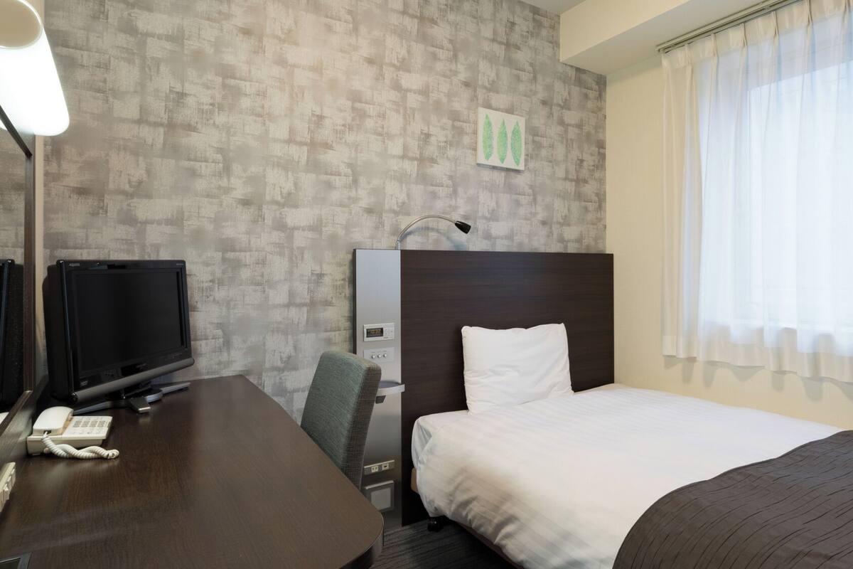 A hotel room with a bed, a desk with a telephone, a television, and a headboard.