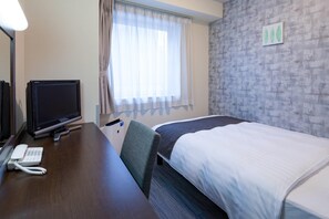 Habitación de hotel con cama, escritorio con monitor de computadora, teléfono y ventana con cortinas.