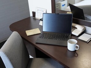 Una laptop sobre un escritorio, con una taza blanca, un teléfono y una pequeña señal.