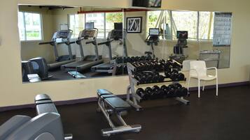 Un gimnasio con cintas de correr, mancuernas y un espejo.