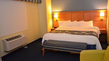A hotel room with a large bed, bedside lamps, a bench, and a wall-mounted air conditioner.