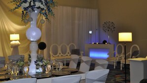 Un coin repas avec des chaises blanches, une table dressée pour le repas et un grand vase rempli de fleurs.