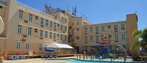 Un hotel con piscina, tumbonas y zona de juegos infantiles.