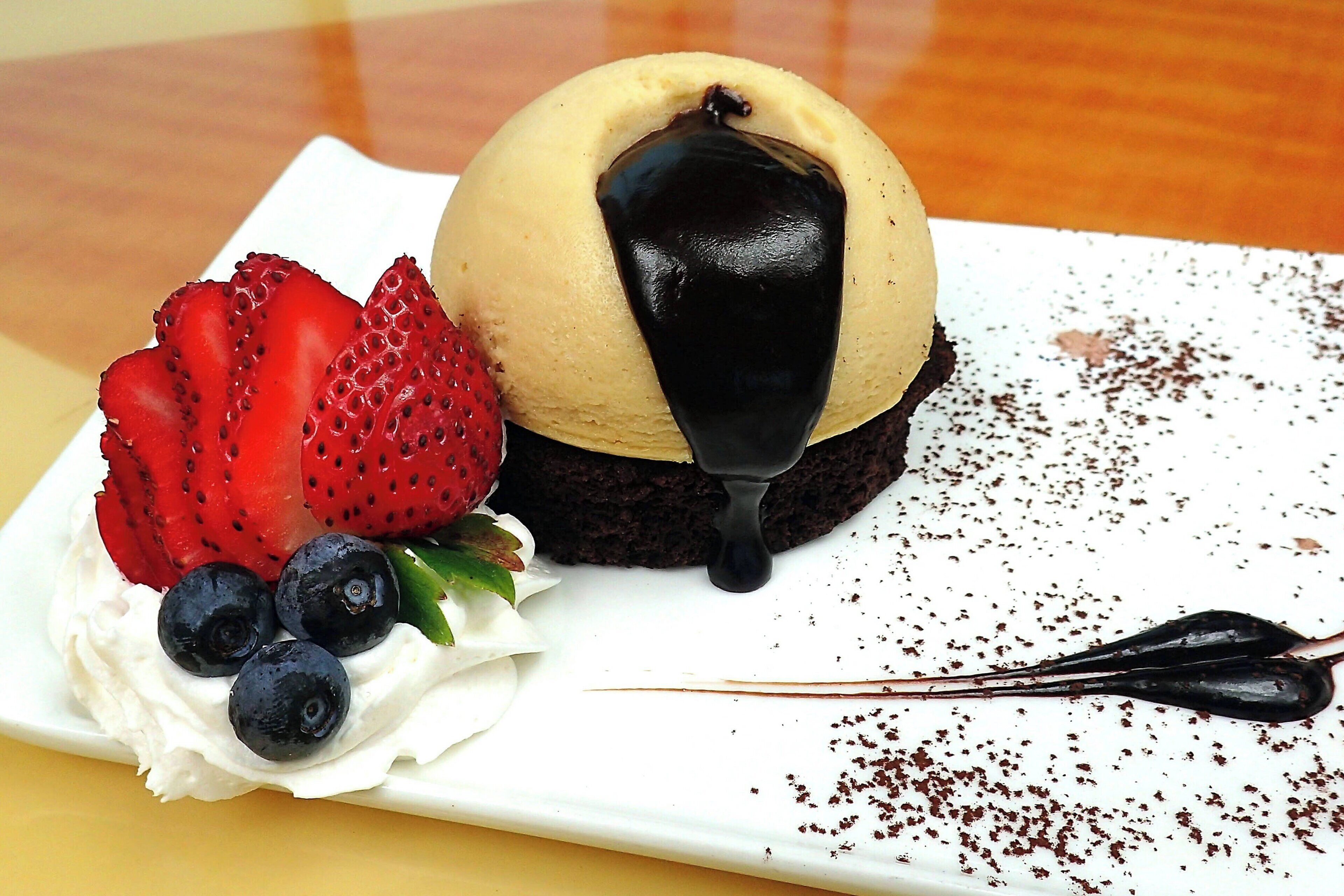 Un postre con fresas, arándanos y salsa de chocolate sobre un plato blanco.