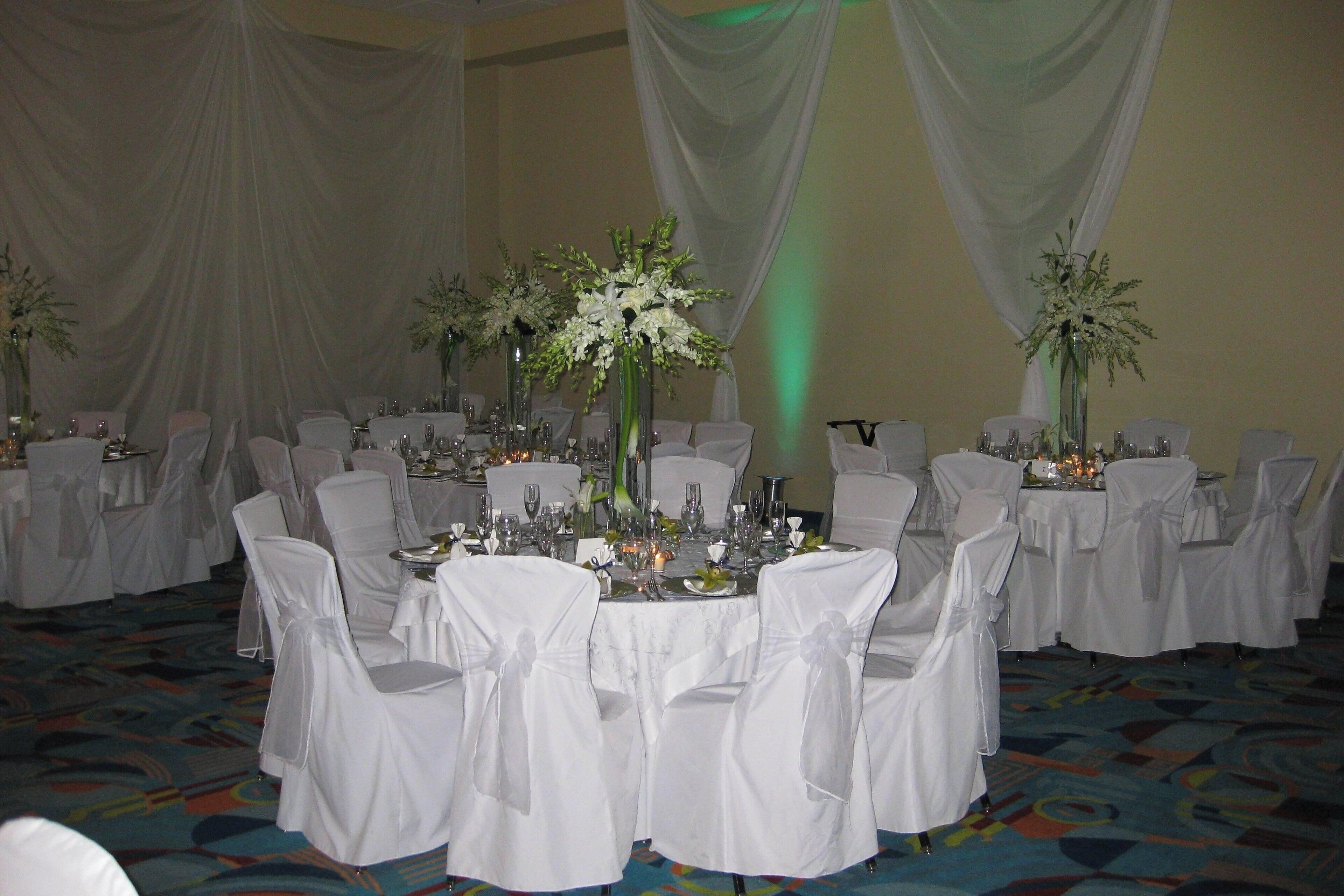 A banquet hall with round tables, white chairs, and floral centerpieces.