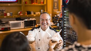 Une personne vêtue d’un uniforme de chef servant des aliments aux clients dans une boulangerie.