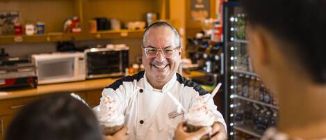 A person in a chef's uniform serving food to customers in a bakery.