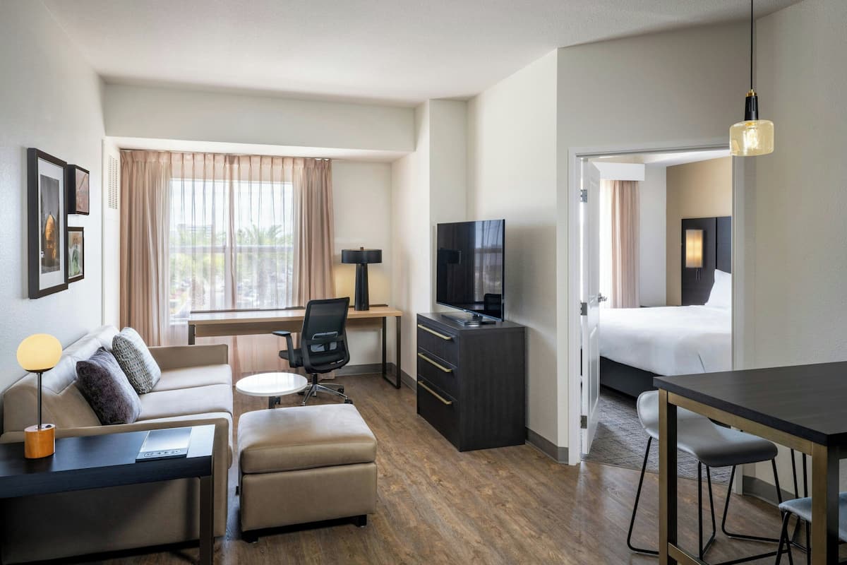 A hotel room with a sofa, a desk, a TV, a bed, and a dining area.
