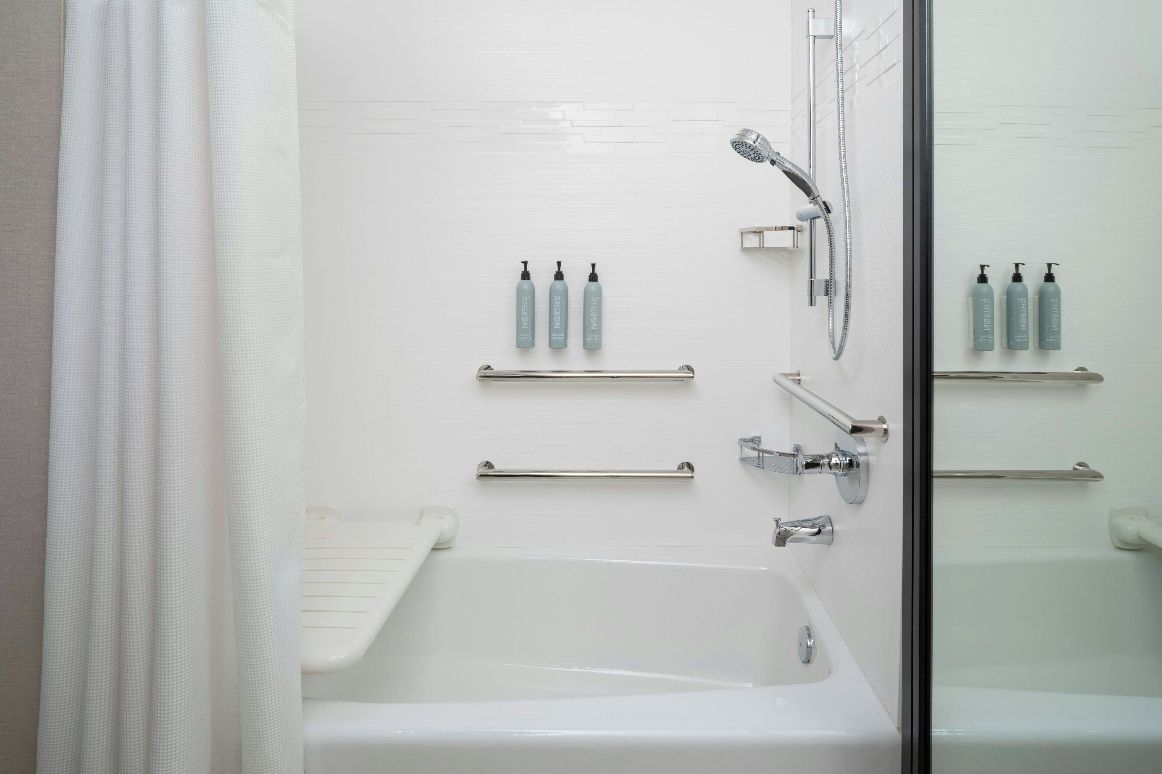 A modern bathroom with a bathtub, shower, and handrails.