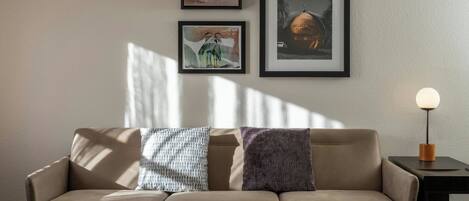 Una sala de estar moderna con un sofá, cuadros enmarcados en la pared y una lámpara de mesa.