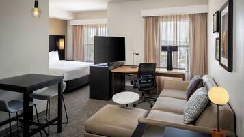 A hotel room with a bed, desk, chair, sofa, and a TV.