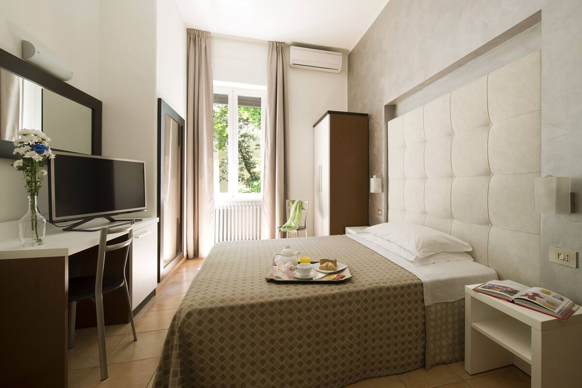 Een hotelkamer met een bed, een televisie, een bureau met een bloevas en een ontbijttray op het bed.