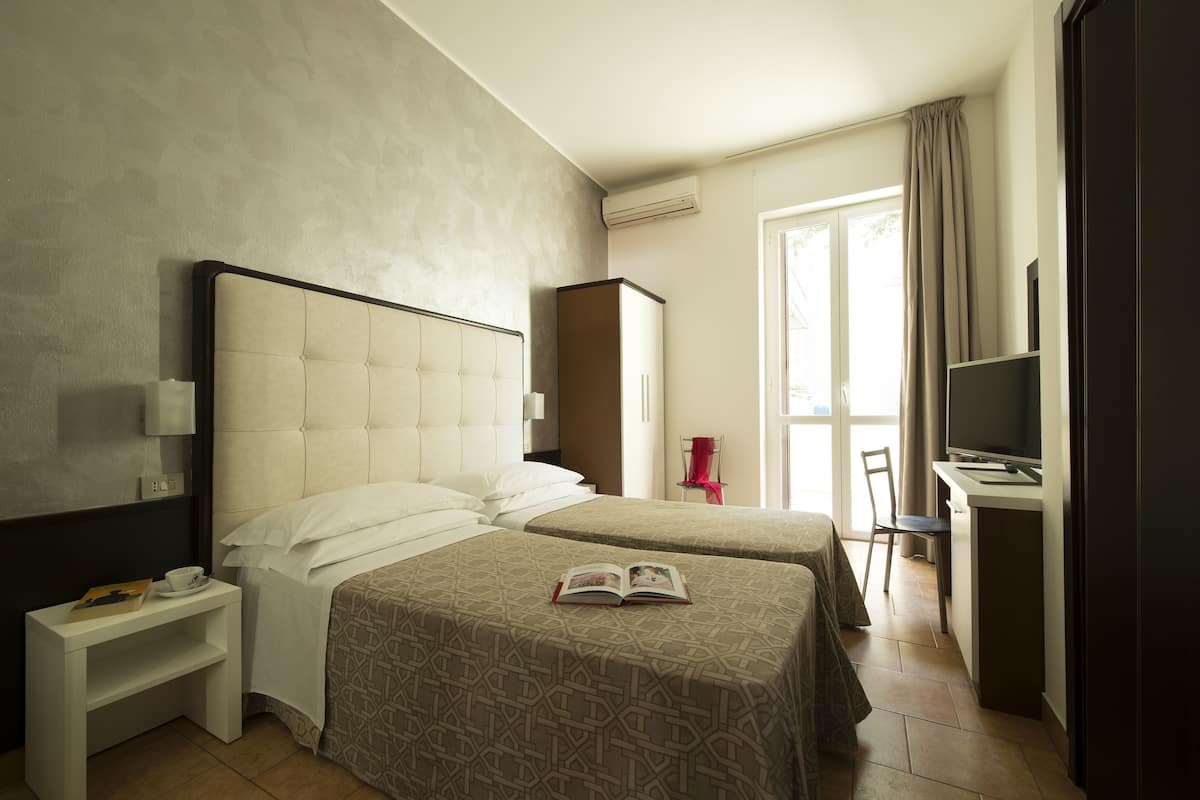 Een hotelkamer met twee bedden, een bureau met stoel, een televisie en een raam met gordijnen.