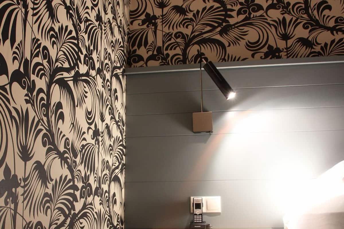 Quarto com papel de parede estampado, mesa de cabeceira com luminária e luminária pendente.