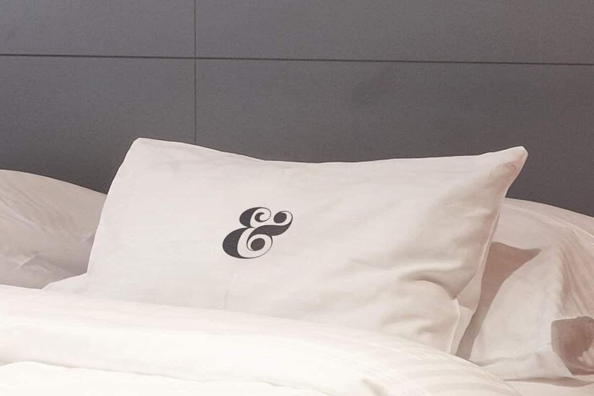 Uma cama com travesseiro branco, cabeceira cinzenta e manta listrada.