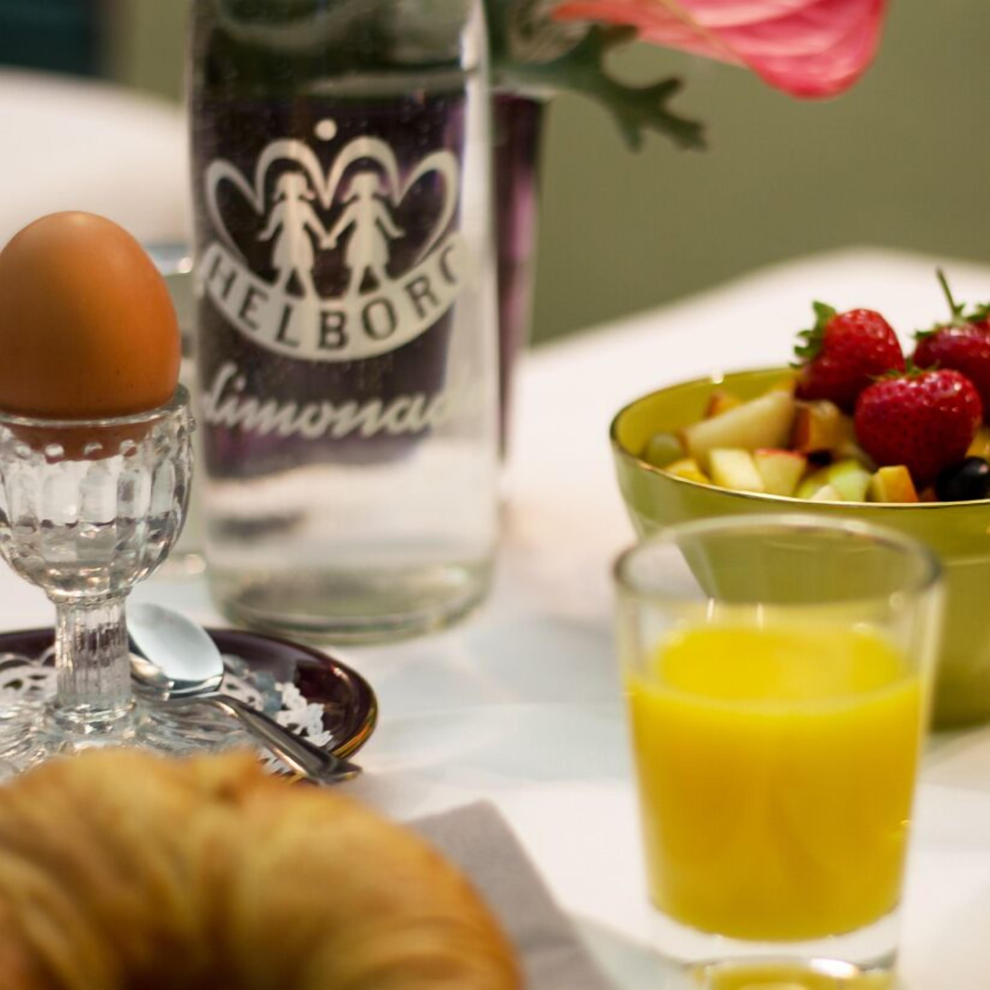 Ein Frühstückstisch mit Orangensaft, einer Obstschale, einem Croissant und einer Flasche Helborg Mineralwasser.