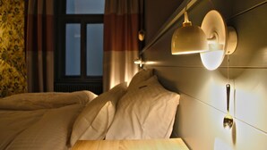 A hotel room with a bed, a nightstand, a wall-mounted lamp, and a window with curtains. - Saint Shermin (Vienna)
