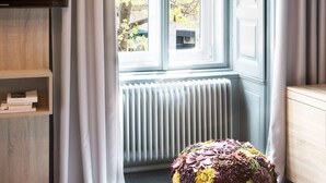A bedroom with a window, a radiator, a TV, and a bookshelf. - Saint Shermin (Vienna)