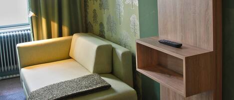 Una habitación con un sofá, un televisor montado en un soporte de madera y un papel tapiz estampado.