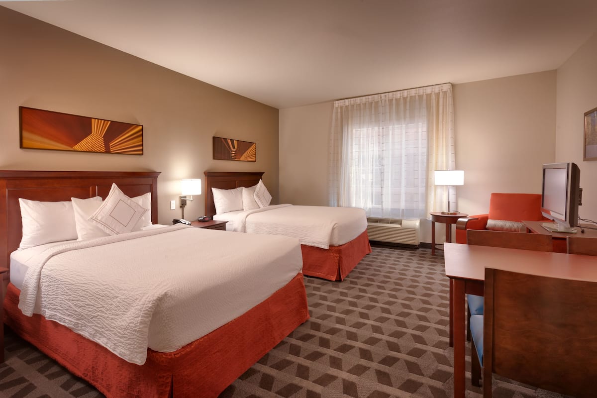 A hotel room with two beds, a desk, a TV, and artwork on the walls.
