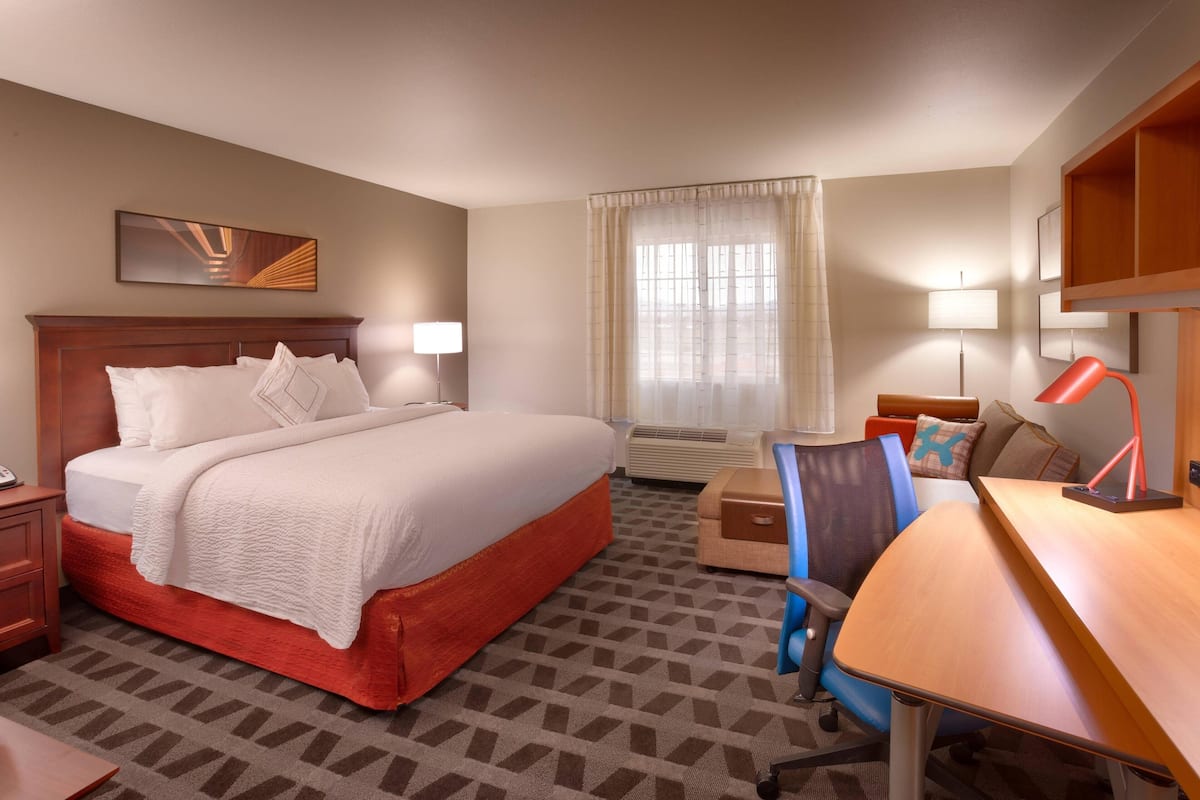 A hotel room with a large bed, a desk, a chair, a lamp, a nightstand, and a window with curtains.