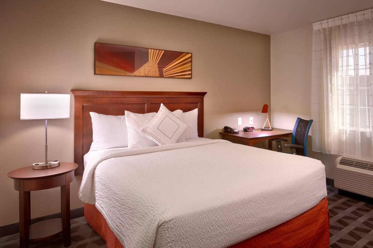 A hotel room with a large bed, a desk, a chair, a lamp, and a painting on the wall.