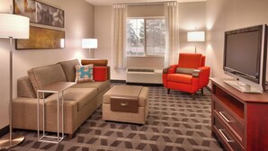 Une chambre d’hôtel équipée d’un canapé, d’un fauteuil, d’un pouf, d’une télévision et d’un appareil de climatisation.