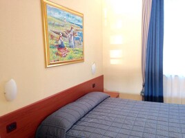 Una habitación de hotel con una cama, un cuadro en la pared y un ventanal con cortinas.