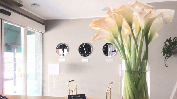 A reception desk with a vase of flowers, clocks labeled 'HOTEL CERVO' and 'TOKYO', and a 'HOTEL' branded keychain.