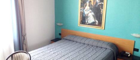 A hotel room with a bed, two bedside tables, a chair, a painting on the wall, and a window with curtains.