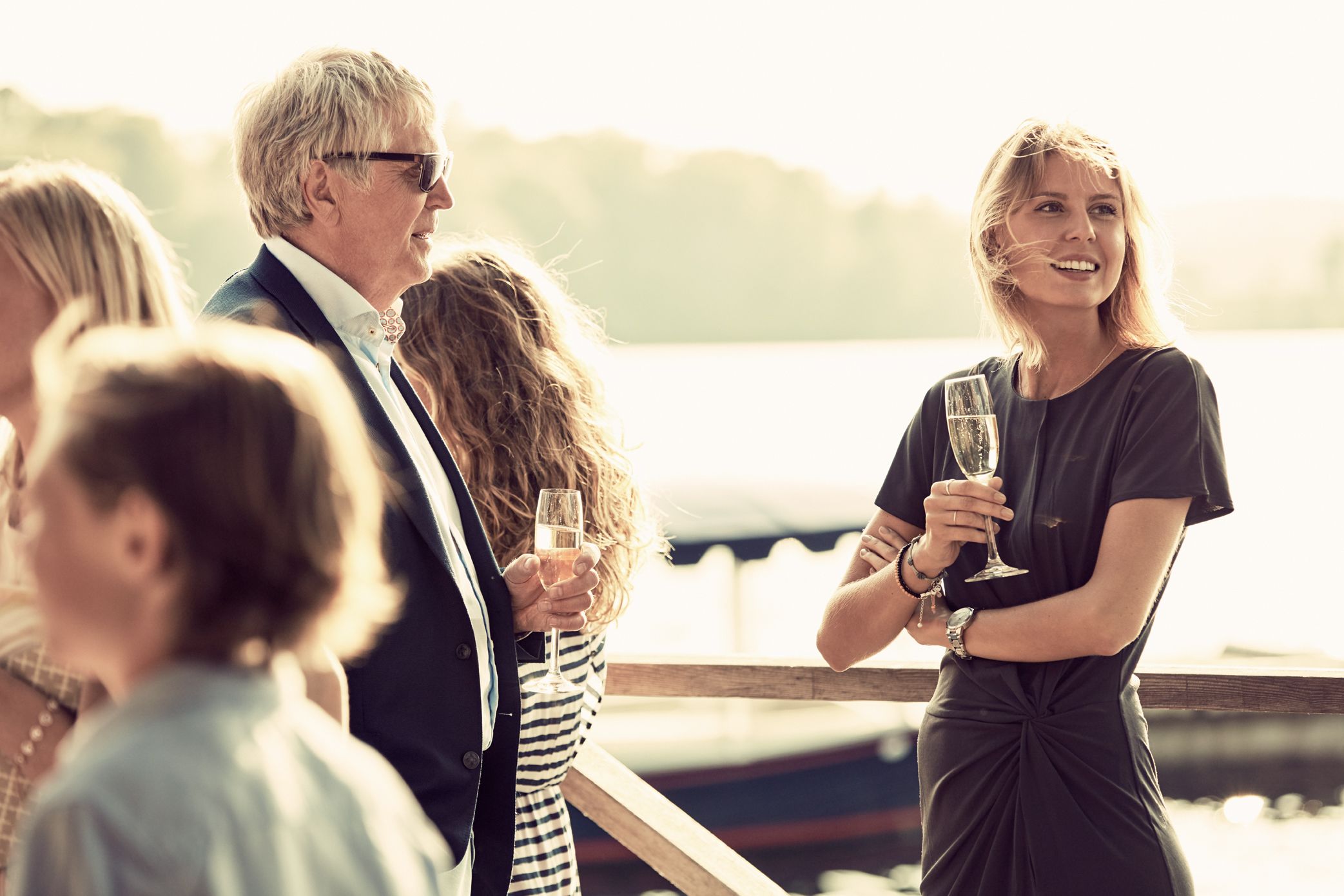 A group of people standing by a waterfront, holding glasses of wine.