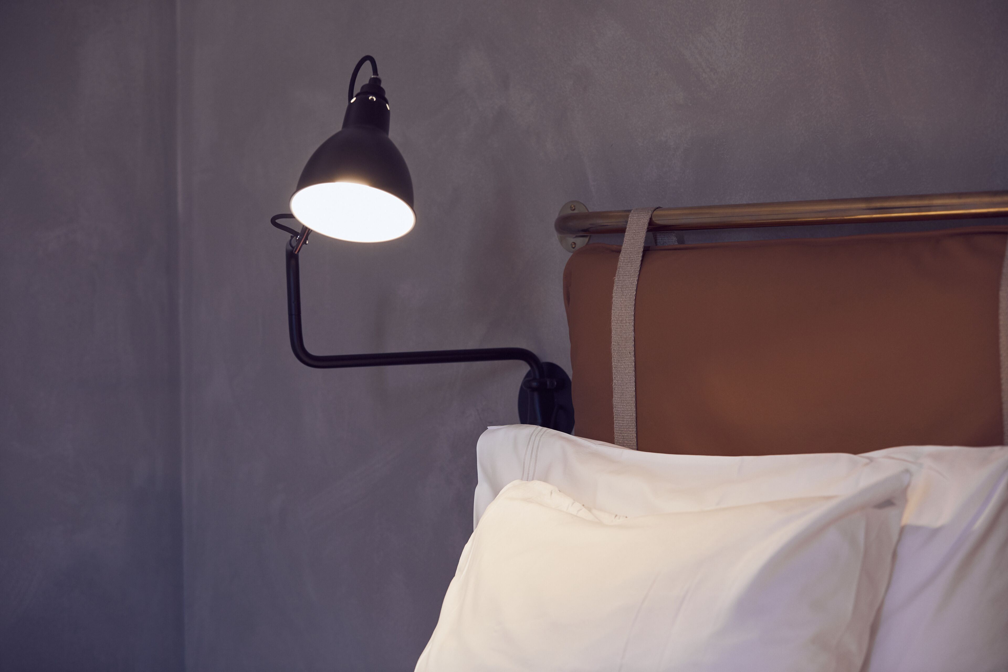 A bed with a headboard, a bedside lamp, and a wall.
