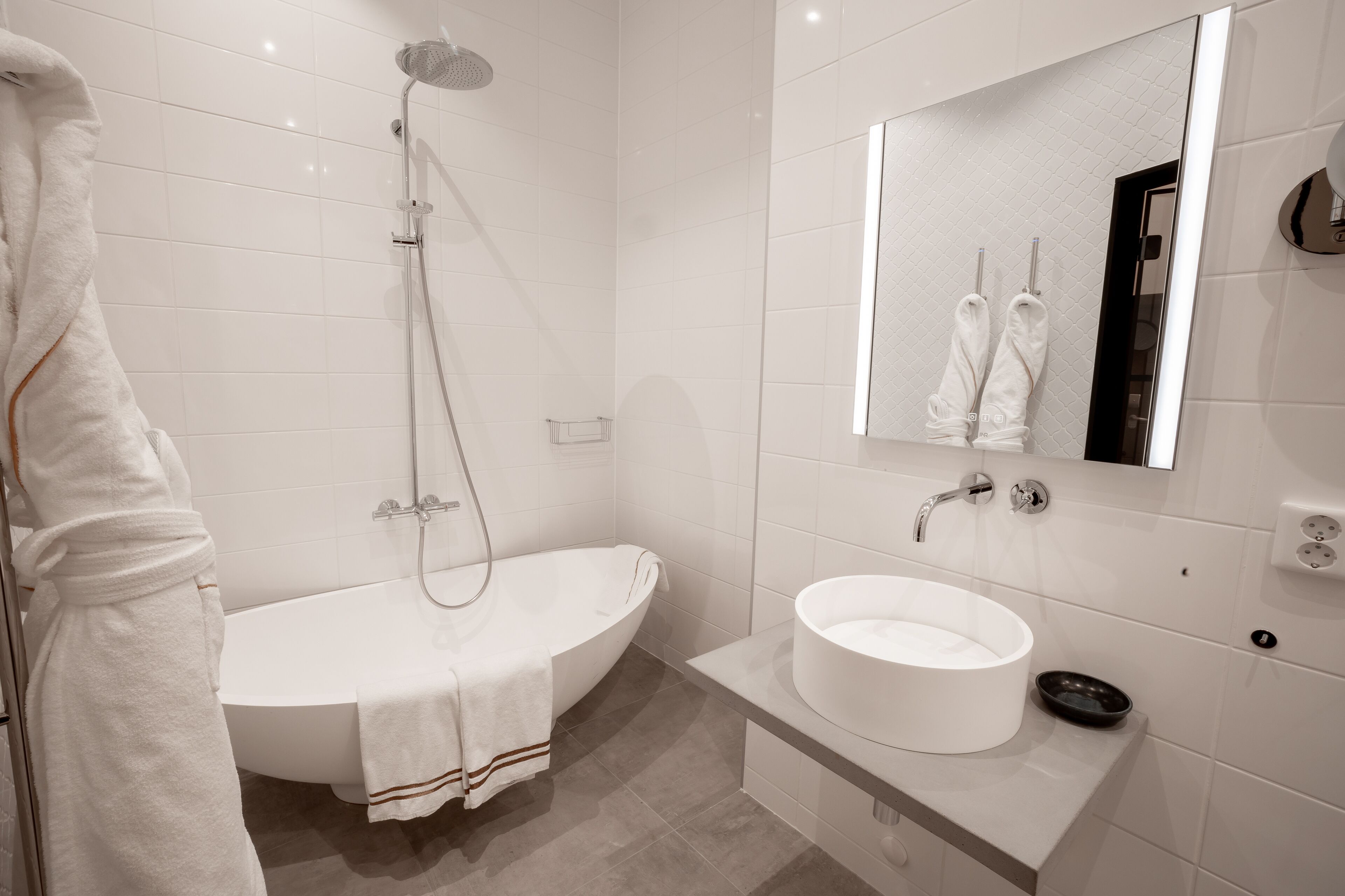 Un baño moderno con una bañera independiente, un espejo grande y un lavamanos blanco.