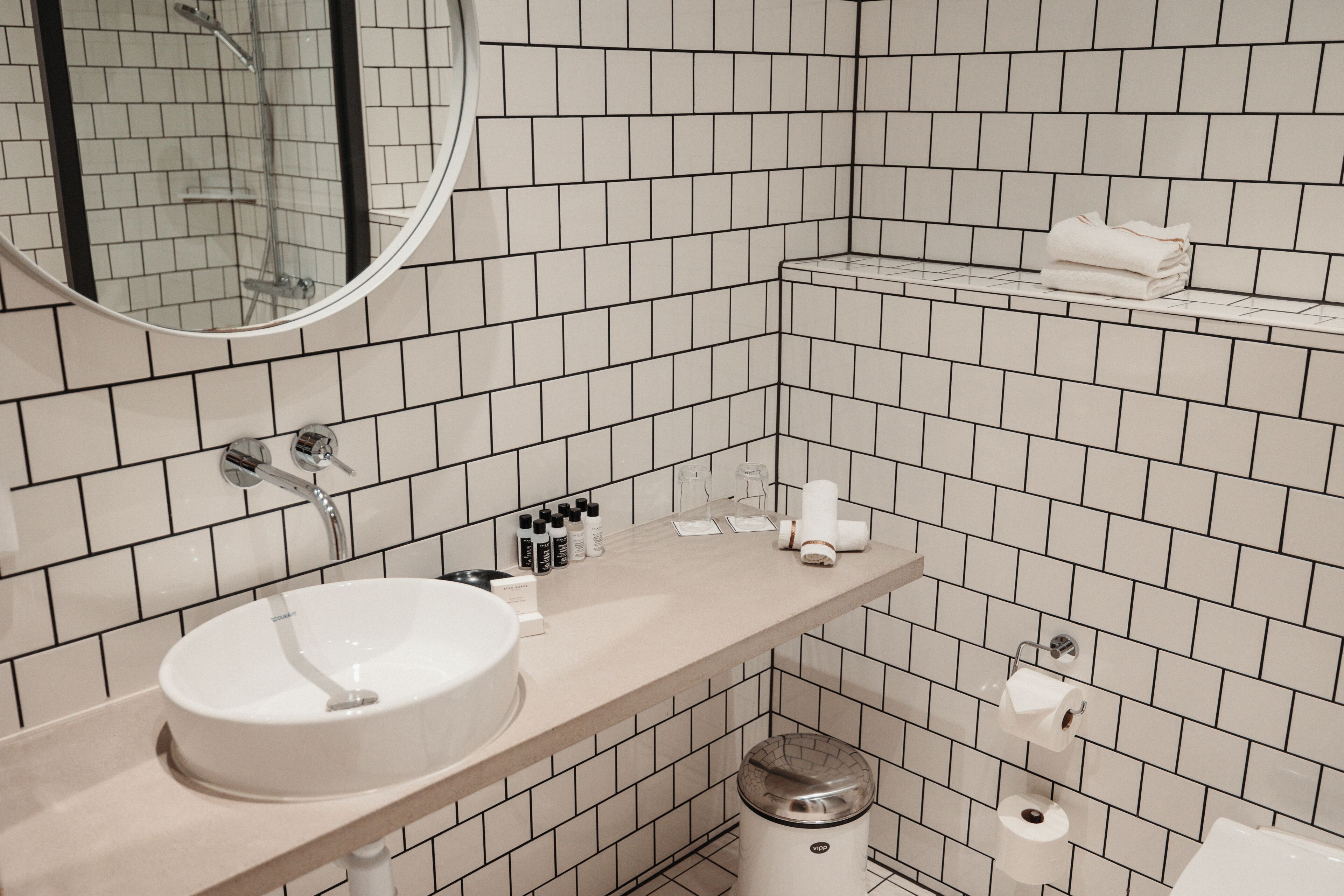 A modern bathroom with a white sink, mirror, and tiled walls.