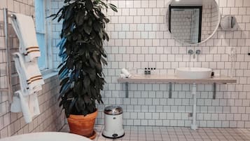 A modern bathroom with white tiled walls, a round mirror, a sink, a toilet, and a potted plant.