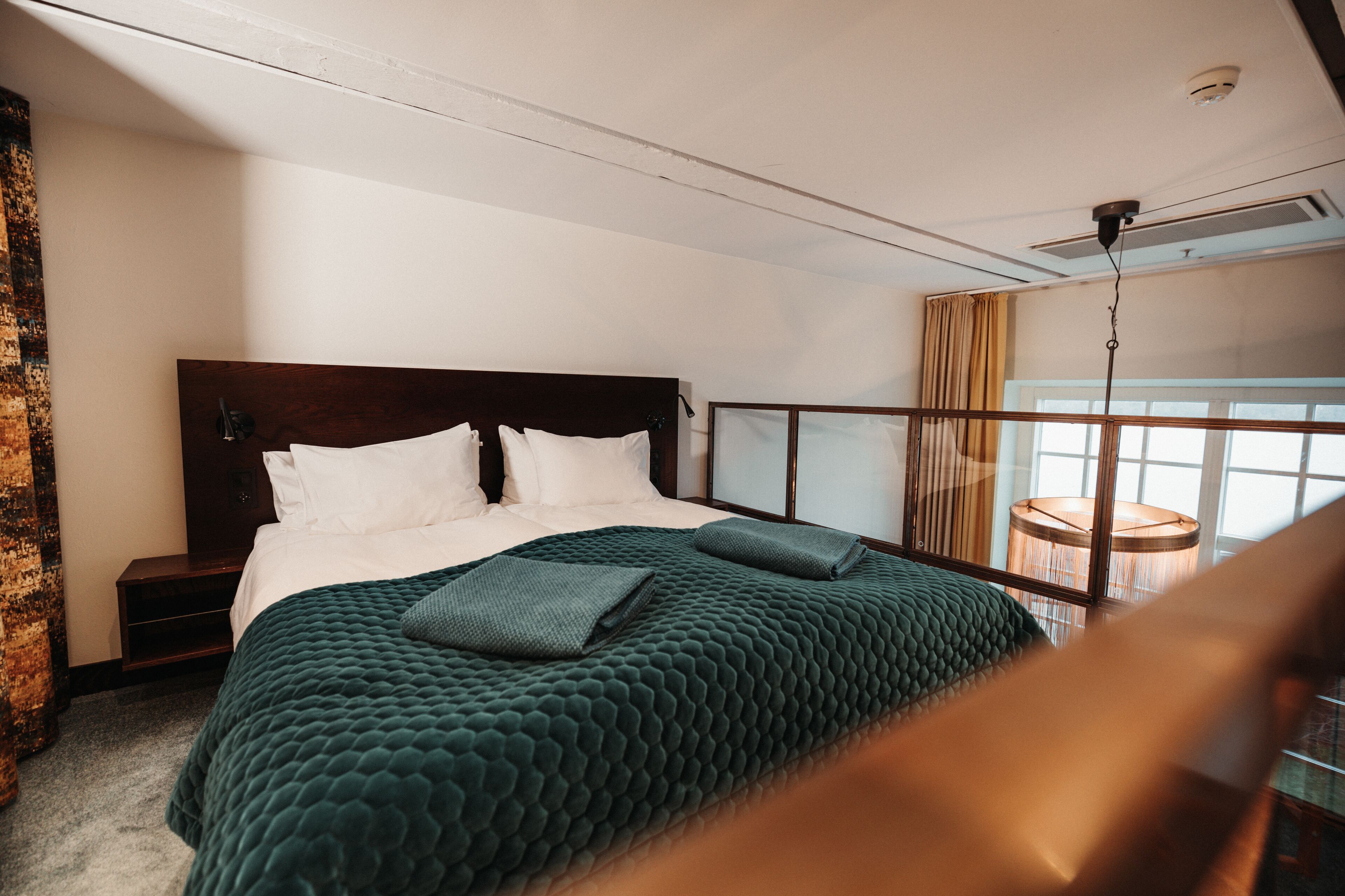 A bedroom with a large bed, a wooden headboard, a nightstand, and a window with curtains.