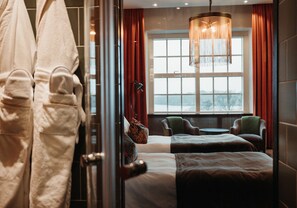 A hotel room with a large window, a chandelier, and two chairs.