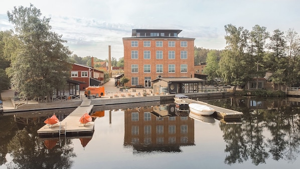 A riverside dock with boats, a red brick building, and a calm water body reflecting the surroundings.