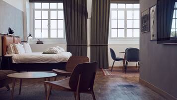 Habitació d'hotel amb un llit, una taula de treball, una cadira i una finestra amb cortines.