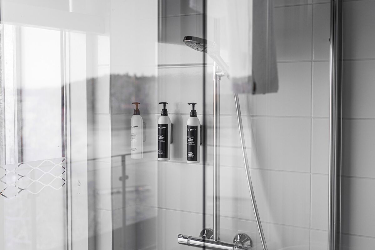 Un baño moderno con cabina de ducha de vidrio, ducha de mano y tres botellas de champú y acondicionador en la pared.